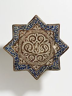 an intricately designed blue and brown plate on a white surface with the shape of a star