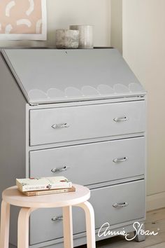 a gray dresser sitting next to a white table with a book on top of it