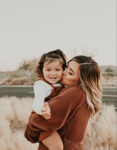 a woman holding a baby in her arms and smiling at the camera while standing next to tall grass