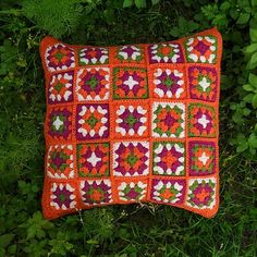 a crocheted pillow sitting on top of green grass next to bushes and plants