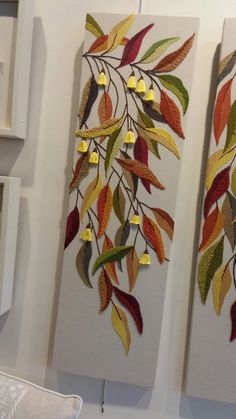 two wall hangings decorated with colorful leaves and gold hearts on white canvases in a room