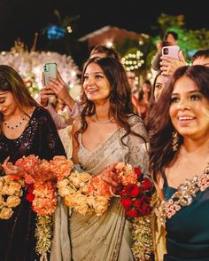 two women in sari are taking pictures with their cell phones at an outdoor event