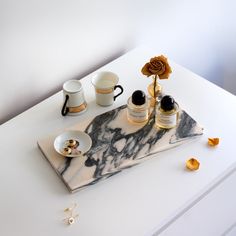 a marble tray with two cups and saucers on it, next to a flower