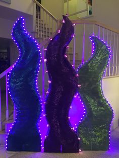 three colorful vases sitting next to each other in front of a stair case with purple and green lights