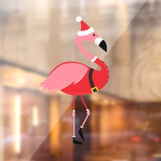 a pink flamingo wearing a santa hat and standing in front of a glass window