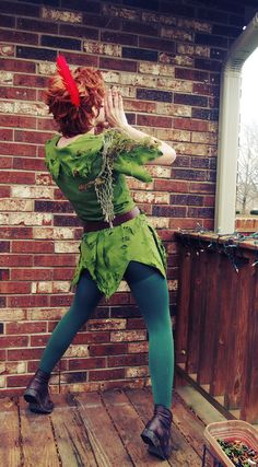 a woman dressed as tinkerbell standing on a wooden deck in front of a brick wall