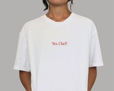 Welcome to Apéro Apparel! Spice up your wardrobe with our exclusive retro-style vintage-fit unisex t-shirt, featuring the slogan "Yes, Chef!". This trendy unisex cut looks great on both women and men. Crafted with 100% high-quality midweight cotton, it's soft to the touch, extra comfy, and durable.   Whether you're a Michelin-star chef, a culinary enthusiast, or just someone who loves to eat, this shirt is sure to add a dash of flavor to your fit. Featuring a classic crew neckline, premium ultra-soft feel, and relaxed fit, it's the perfect addition to your streetwear wardrobe essentials.   Product Details:   * Made with 100% midweight 6.1oz cotton * Soft-to-the-touch feel for ultimate comfort * Pre-shrunk for a consistently great fit * Classic crew neckline for a timeless look * Tear-away White T-shirt With Funny Text For Streetwear, Unisex Text Print Crew Neck T-shirt, Unisex Crew Neck T-shirt With Text Print, Unisex Retro T-shirt With Text Print, Unisex Crew Neck Graphic Tee Shirt, Unisex Graphic Tee With Crew Neck, Unisex Text Print T-shirt With Crew Neck, Unisex Retro Crew Neck T-shirt, Graphic Tee With Slogan Crew Neck