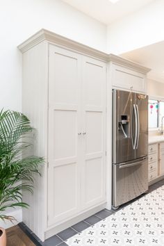 a kitchen with white cabinets and a stainless steel refrigerator in the center, next to a potted plant