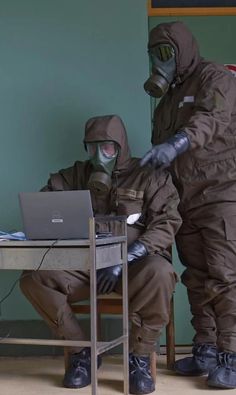 two people in protective gear sitting at a table with a laptop computer on their laps