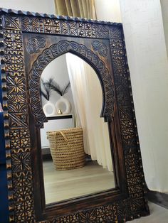 an ornate wooden mirror sitting on top of a table next to a basket and vase