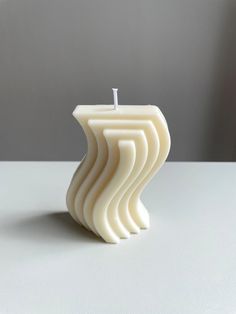 a white candle sitting on top of a table next to a gray and white wall