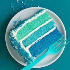 a piece of blue and green cake on a plate with a fork next to it