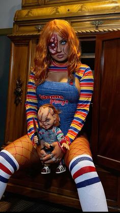 a woman sitting on top of a wooden cabinet holding a doll with blood all over her face