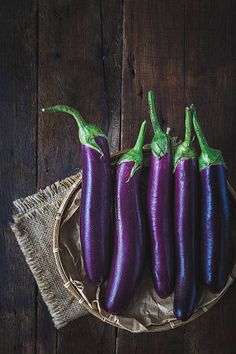 three purple eggplant's sitting on a wooden table next to a cloth