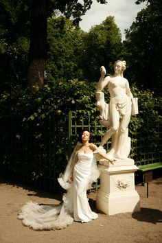 a woman in a wedding dress standing next to a statue