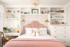 a bedroom with pink bedding and white shelving, two teddy bears sitting on the bed