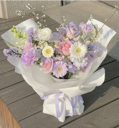 a bouquet of flowers sitting on top of a wooden table next to a bench with white and pink flowers