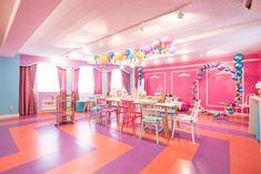 a brightly colored room with tables, chairs and balloons hanging from the ceiling in front of windows