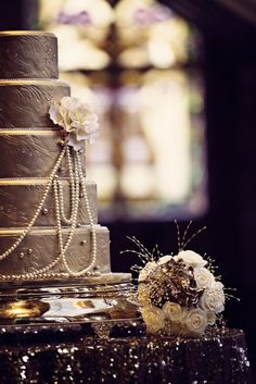 a three tiered cake with flowers and pearls on the top is sitting on a table