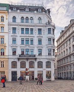 people are walking around in front of a large white building with lots of windows and balconies