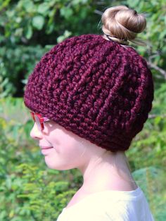 a woman wearing a knitted beanie with a ponytail in her hair and glasses