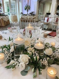 an arrangement of flowers and candles on a table in a room with white linens