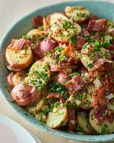 a blue bowl filled with potatoes and bacon on top of a wooden table next to a fork