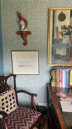 a chair and desk in a room with blue wallpaper, framed pictures on the wall