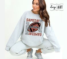 a woman is sitting on the ground wearing a sweatshirt and sweatpants that says gameday weekend