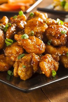 chicken wings with sauce and green onions on a black plate