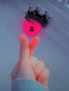 a person's hand is touching the letter s in front of a pink heart