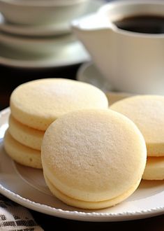 three cookies on a white plate next to a cup of coffee and saucer in the background