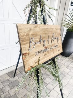 a wooden sign sitting on top of a metal stand next to a potted plant