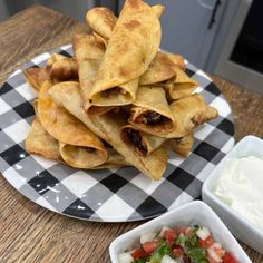 some tacos are sitting on a plate next to a bowl of sour cream and dip