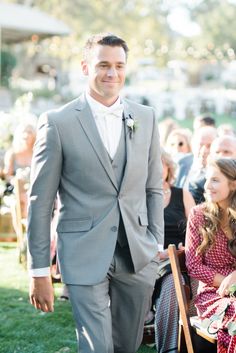 a man in a gray suit and tie walking down the aisle at a wedding ceremony