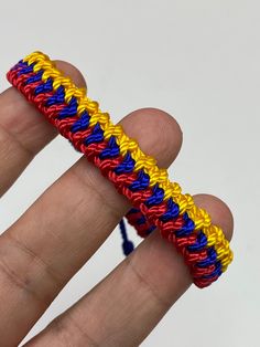 a hand is holding a multicolored rainbow loom bracelet on it's thumb