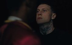 a man with tattoos on his neck looking at another man's face in the dark