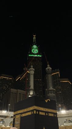 the clock tower is lit up at night in front of some tall buildings with lights on them