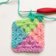 a crocheted granny square with a red handled knitting needle next to it on a white surface