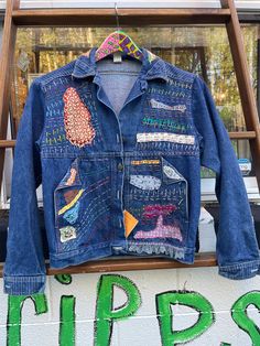 a denim jacket with patches hanging on a clothes rack in front of a sign that says tips