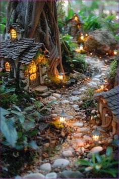 a fairy garden is lit up with candles and lights in the trees, along with small houses