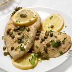 two pieces of chicken with capers and lemons on a white plate