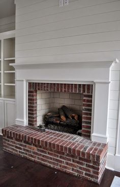 an empty living room with a brick fireplace and built in bookcases on either side