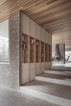 an empty room with bookshelves and stairs leading up to the second floor, in front of a brick wall