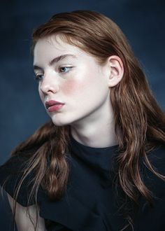 a woman with long hair and blue eyes is posing for a photo in front of a dark background