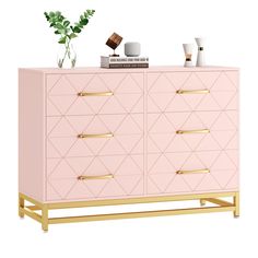 a pink dresser with gold handles and drawers on it, next to a potted plant