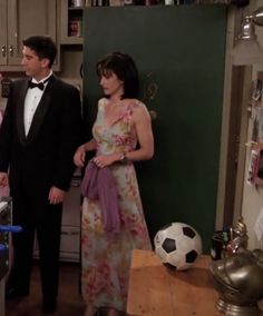 two people standing in a kitchen with a soccer ball on the counter and cabinets behind them