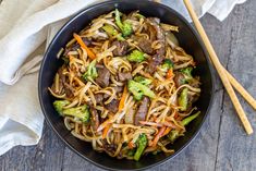 a bowl filled with beef and noodles on top of a wooden table next to chopsticks