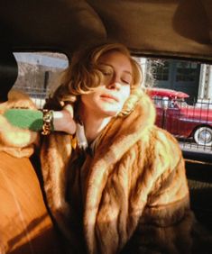 a woman sitting in the back seat of a car wearing a fur coat and gold bracelets