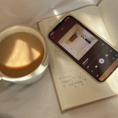 a cup of coffee sitting next to an open book and cell phone on top of a table